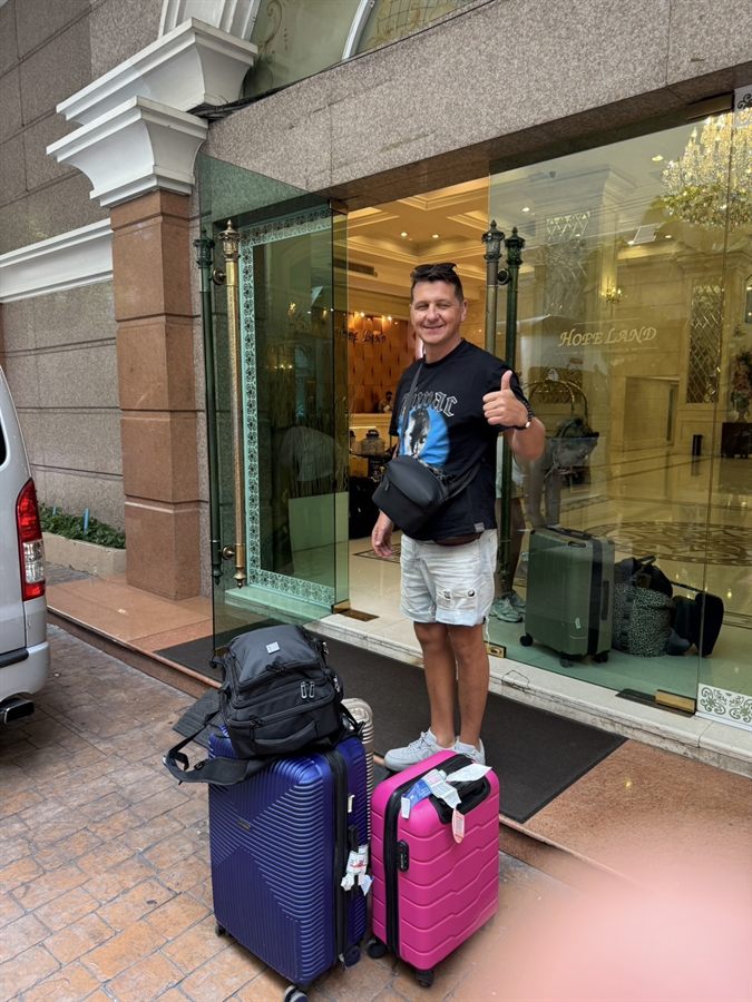 A guest with two suitcases at his hotel entrance beside a WayGo van in Bangkok.