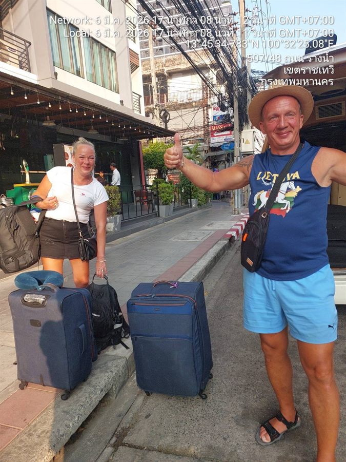 Two guests with their suitcases on a Bangkok street beside a WayGo van in Ratchathewi.